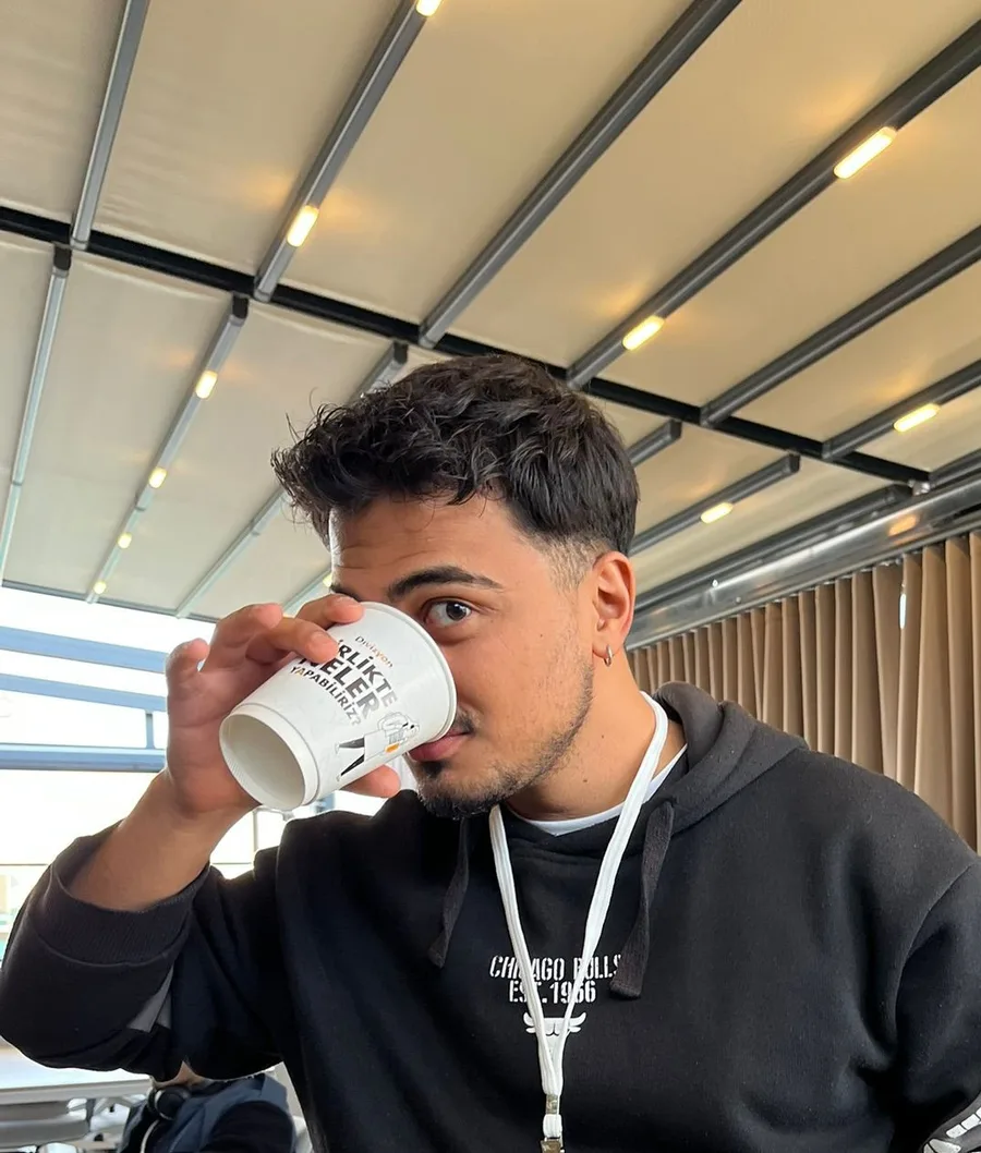 Muhammed Ali Bilgin drinking coffee from a paper cup, wearing a black hoodie